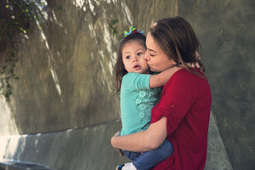 Mother kissing daughter while standing at park - CAVF20071