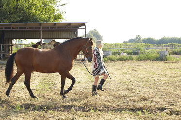 Frau hält Pferd und geht auf einem Bauernhof spazieren - CAVF20085