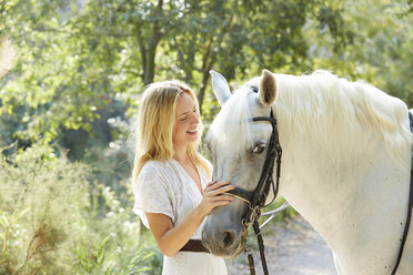 Glückliche Frau streichelt weißes Pferd auf dem Bauernhof - CAVF20088