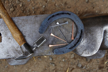 Draufsicht auf ein Hufeisen mit Hammer und Nägeln auf einem Amboss - CAVF20101