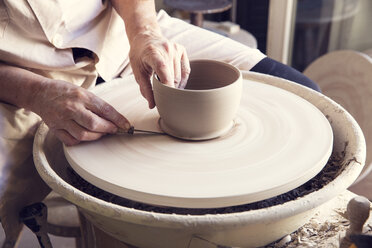 Woman molding shape to clay with work tool on pottery wheel - CAVF20113