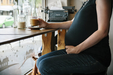 Midsection of pregnant woman having coffee while sitting by window in cafe - CAVF20162