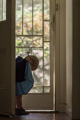 Side view of baby girl looking at her dress white standing by door in house - CAVF20166