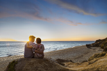 Rückansicht eines Paares, das auf einem Felsen am Strand sitzt, gegen den Himmel bei Sonnenuntergang - CAVF20172