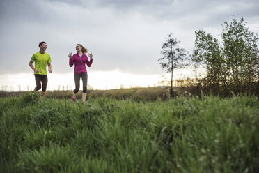 Happy friends talking while jogging on grassy field - CAVF20192