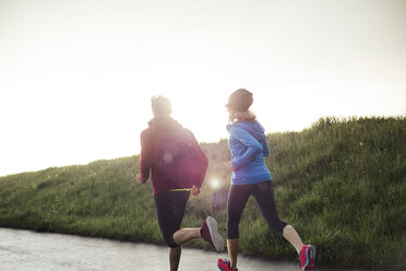 Rear view of friends running on road by grassy field during sunset - CAVF20202