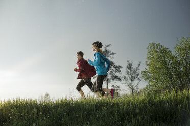 Side view of determined athletes running on grassy field during sunset - CAVF20207