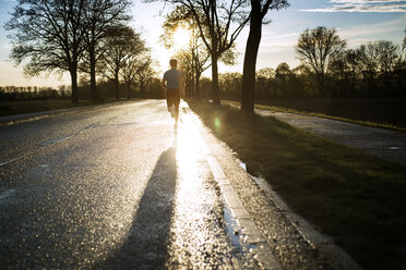 Rückansicht eines männlichen Sportlers, der bei Sonnenuntergang auf der Straße läuft - CAVF20222