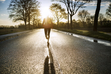 Rückansicht eines weiblichen Sportlers, der bei Sonnenuntergang auf der Straße läuft - CAVF20223