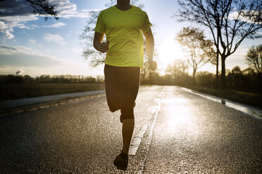 Tiefschnitt eines entschlossenen männlichen Sportlers, der bei Sonnenuntergang auf der Straße läuft - CAVF20226