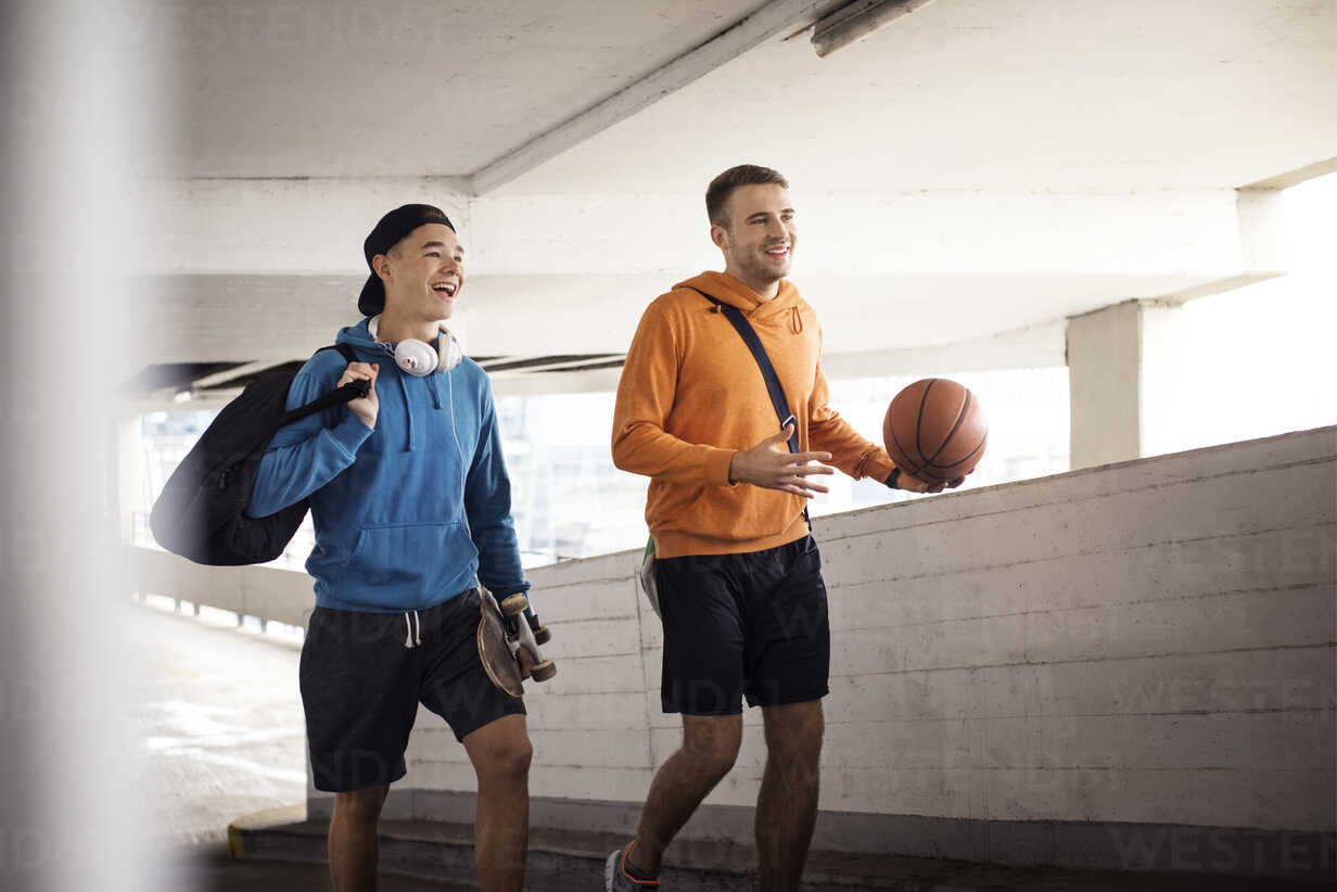 Cheerful male friends holding basketball and skateboard while