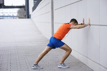 Seitenansicht eines männlichen Sportlers, der sich beim Training auf dem Gehweg an die Wand lehnt - CAVF20259