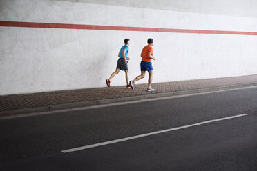 Rear view of male athletes running on sidewalk by road - CAVF20262