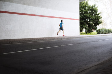 Rückansicht eines männlichen Sportlers, der auf dem Gehweg neben der Straße läuft - CAVF20263