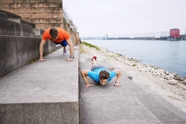 Entschlossene männliche Sportler machen Liegestütze auf Stufen am Strand - CAVF20270