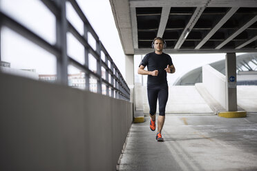 Determined male athlete running in parking lot - CAVF20276