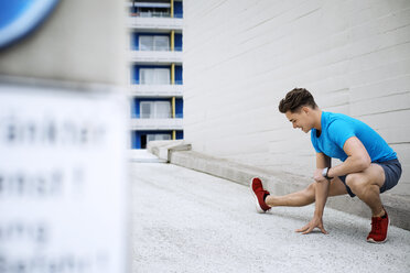 Entschlossener männlicher Sportler bei einer Adduktorendehnungsübung auf der Terrasse - CAVF20285