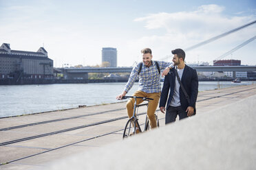 Glücklicher Mann auf dem Fahrrad neben einem Freund, der gegen den Himmel läuft - CAVF20299