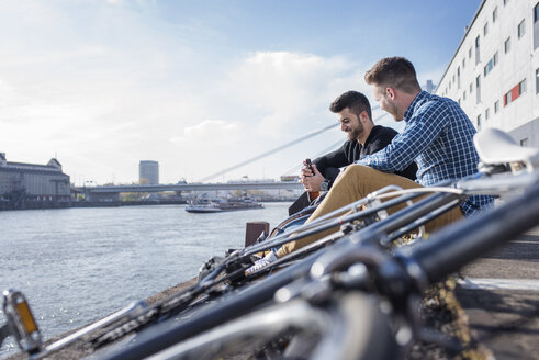 Freunde sitzen mit dem Fahrrad vor einem Kanal gegen den klaren Himmel - CAVF20302