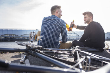 Freunde stoßen mit einer Bierflasche an, während sie mit dem Fahrrad auf der Promenade gegen den klaren Himmel sitzen - CAVF20303