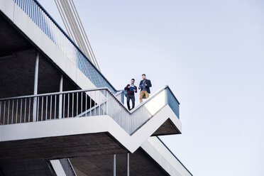 Niedriger Blickwinkel von Männern, die auf den Stufen einer Brücke gegen den klaren Himmel laufen - CAVF20308