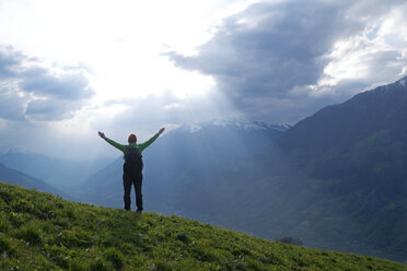 Rear view of female hiker standing with arms outstretched on mountain against cloudy sky - CAVF20330