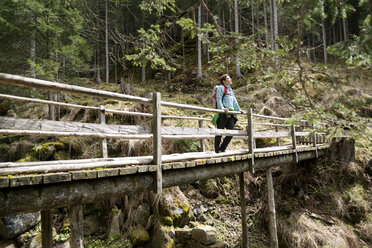 Female hiker standing on footbridge in forest - CAVF20334