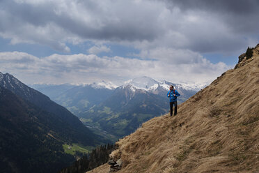 Thoughtful male hiker standing on mountain against cloudy sky - CAVF20338