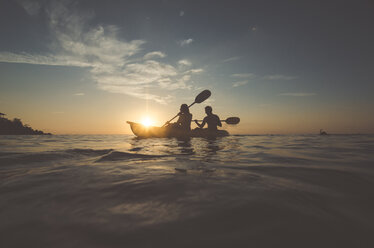 Silhouette friends sitting in kayak on sea against sky during sunset - CAVF20380