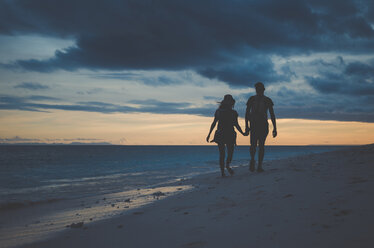 Silhouette couple holding hands and walking at beach against cloudy sky during sunset - CAVF20381