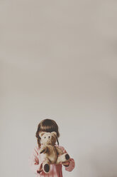 Girl holding teddy bear in front of face against white wall - CAVF20388