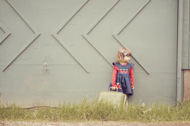 Girl holding suitcase while standing against wall - CAVF20390