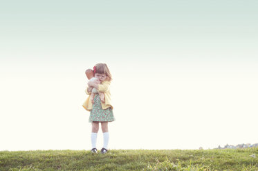 Niedliches Mädchen, das eine Puppe umarmt, während es auf einem Feld gegen den klaren Himmel steht - CAVF20396