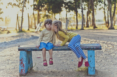 Girl kissing sister while sitting on bench at park - CAVF20409
