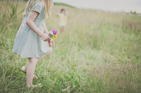 Seitenansicht eines Mädchens, das Blumen auf einem Feld hält, mit einer Schwester im Hintergrund - CAVF20414