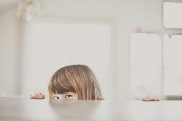 Portrait of girl peeking over table at home - CAVF20424