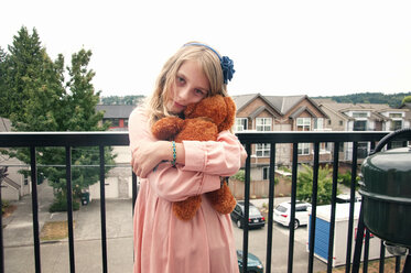 Porträt eines Mädchens, das einen Teddybär hält und auf einem Balkon steht - CAVF20440
