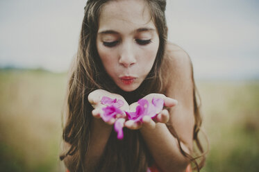 Cute girl blowing pink flower petals on field - CAVF20448