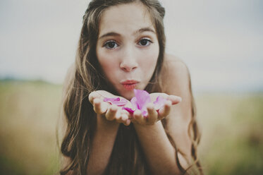Portrait of happy girl blowing pink flower petals on field - CAVF20449