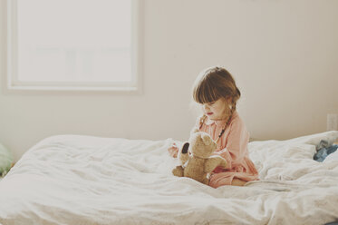 Nettes Mädchen spielt mit Teddybär auf Bett - CAVF20462