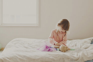 Mädchen spielt mit Teddybär auf Bett - CAVF20463
