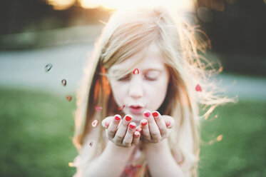 Cute girl blowing heart shapes at park - CAVF20473