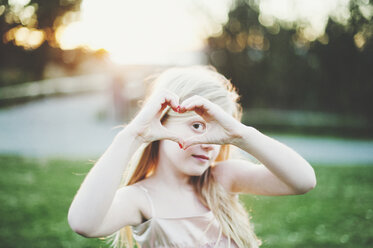 Porträt eines Mädchens, das im Park aus den Händen ein Herz formt - CAVF20474