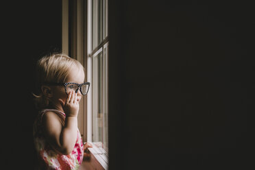 Baby girl wearing eyeglasses while looking through window - CAVF20504