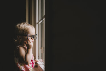 Ein kleines Mädchen trägt eine Brille und schaut durch ein Fenster - CAVF20504