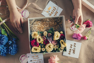 Draufsicht auf einen Floristen, der Blumen in einer Schachtel auf einem Tisch im Blumenladen arrangiert - CAVF20518