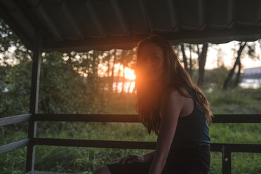Frau schaut weg, während sie bei Sonnenuntergang auf der Veranda sitzt - CAVF20520