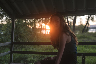 Woman looking away while sitting in porch during sunset - CAVF20520