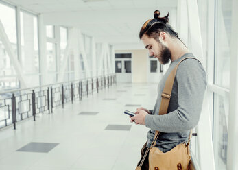 Seitenansicht eines Mannes, der ein Mobiltelefon benutzt, während er im Korridor steht - CAVF20522