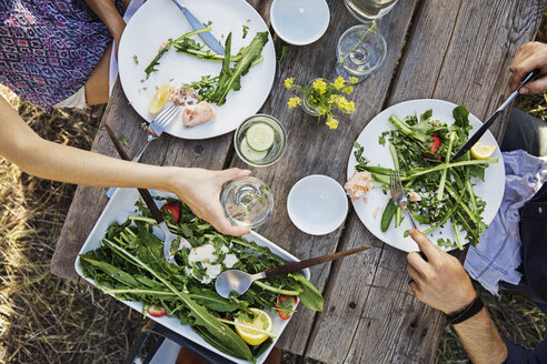 Cropped image of man and woman eating arugula salad at table - CAVF20555